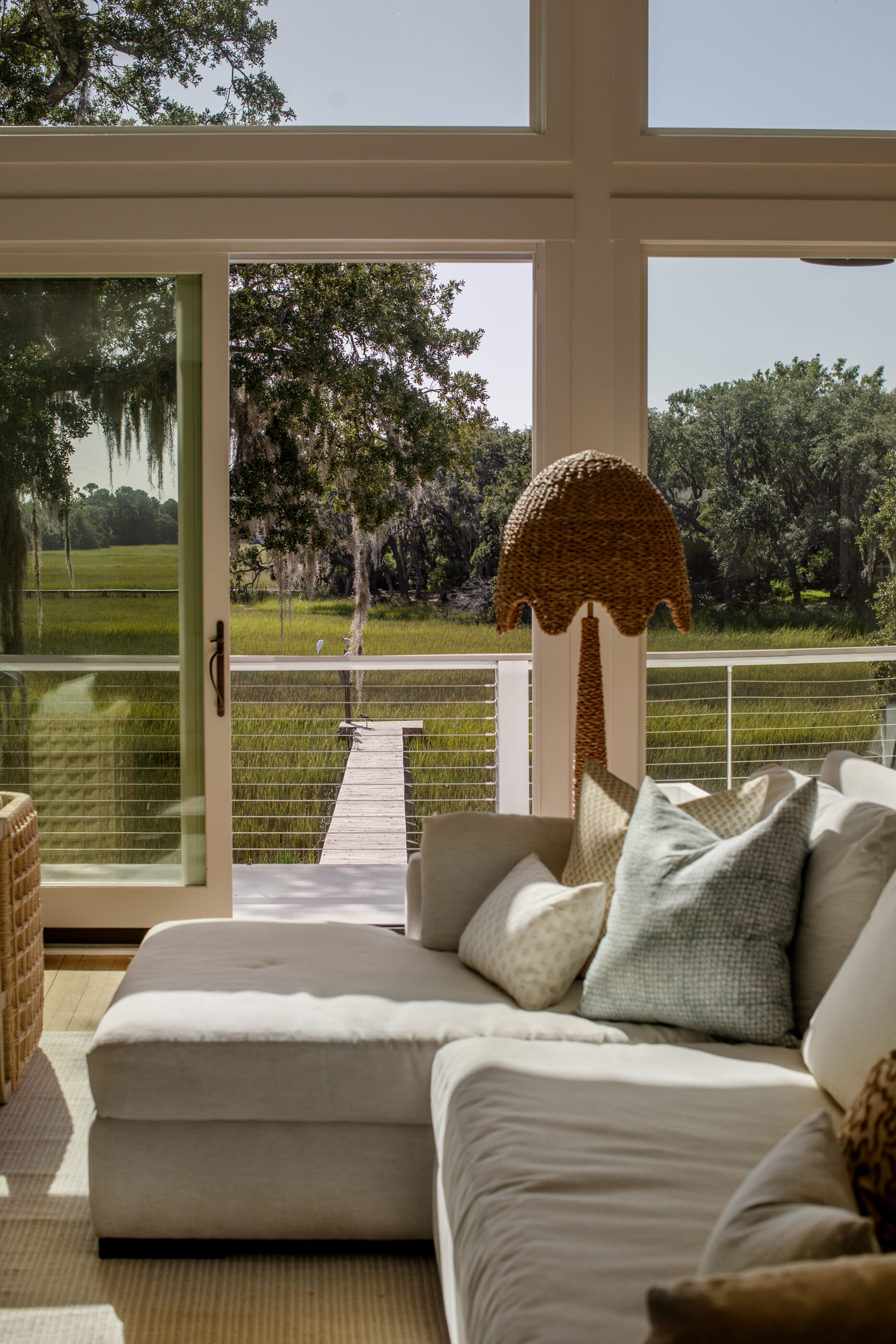 Coastal luxury living room by Megan Molten featuring a neutral sectional sofa, layered textured pillows, woven floor lamp, and expansive windows overlooking the Charleston Lowcountry marsh.