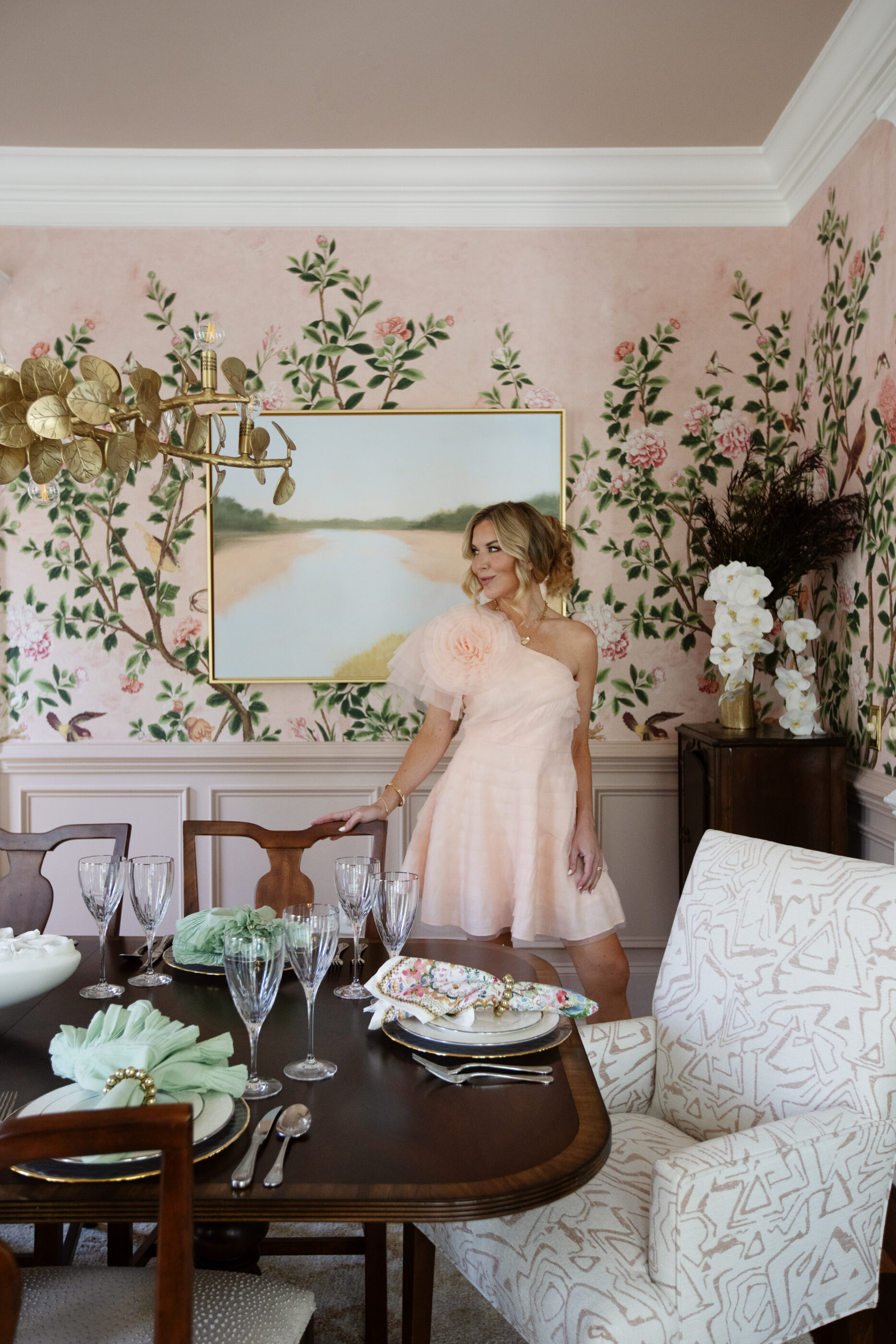Feminine dining room with blush floral wallpaper mural, brass chandelier, dark wood dining table, and layered tablescape in a Charleston coastal luxury home by Megan Molten.