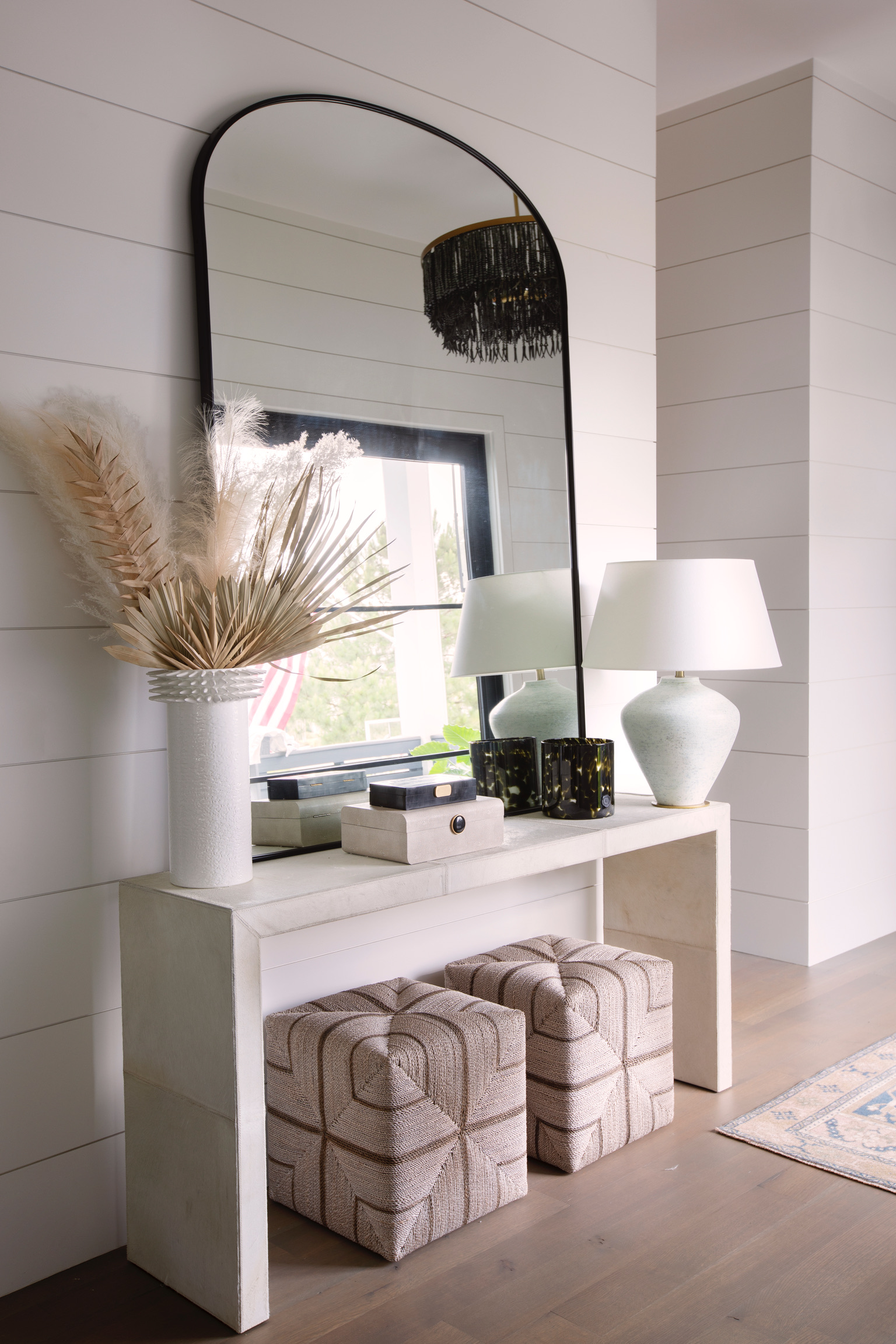 Coastal luxe entryway with neutral console table, arched mirror, soft lighting, and dried palm décor for a resort-style home feel