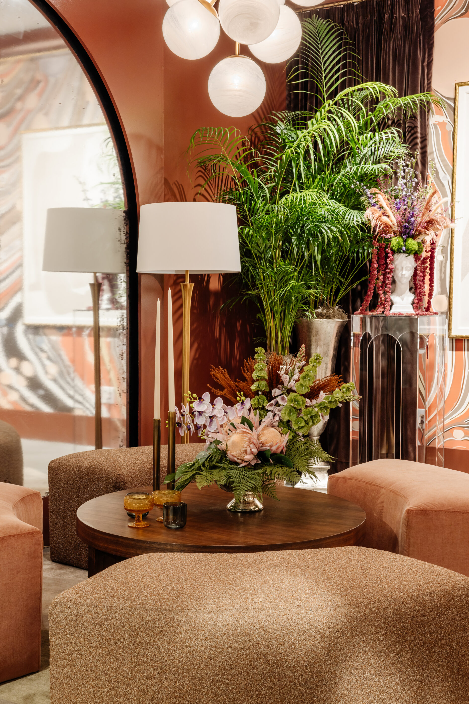 Moody designer living room with a round wood coffee table, floral arrangement, candles, greenery, and warm-toned decor