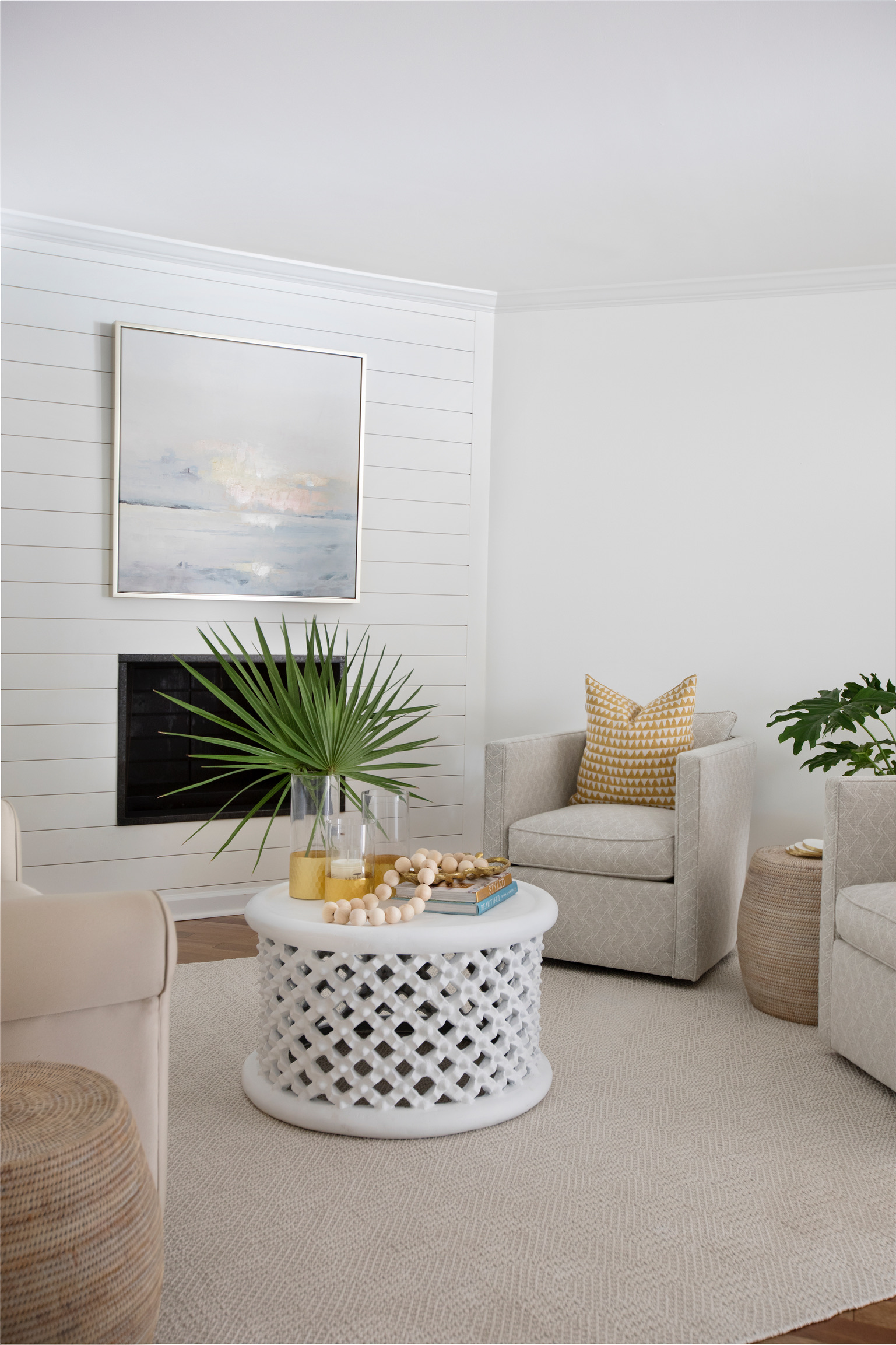 Modern coastal living room with a white lattice coffee table, neutral chairs, palm leaves, books, and woven accents