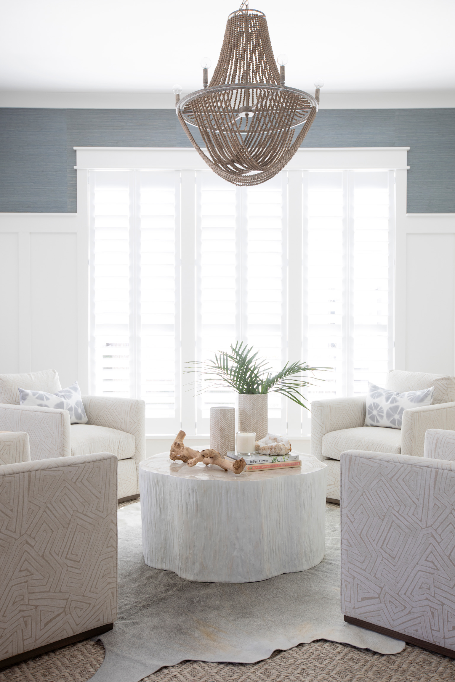 Light and airy living room with a round white coffee table, coastal decor, palm leaves, and a woven chandelier