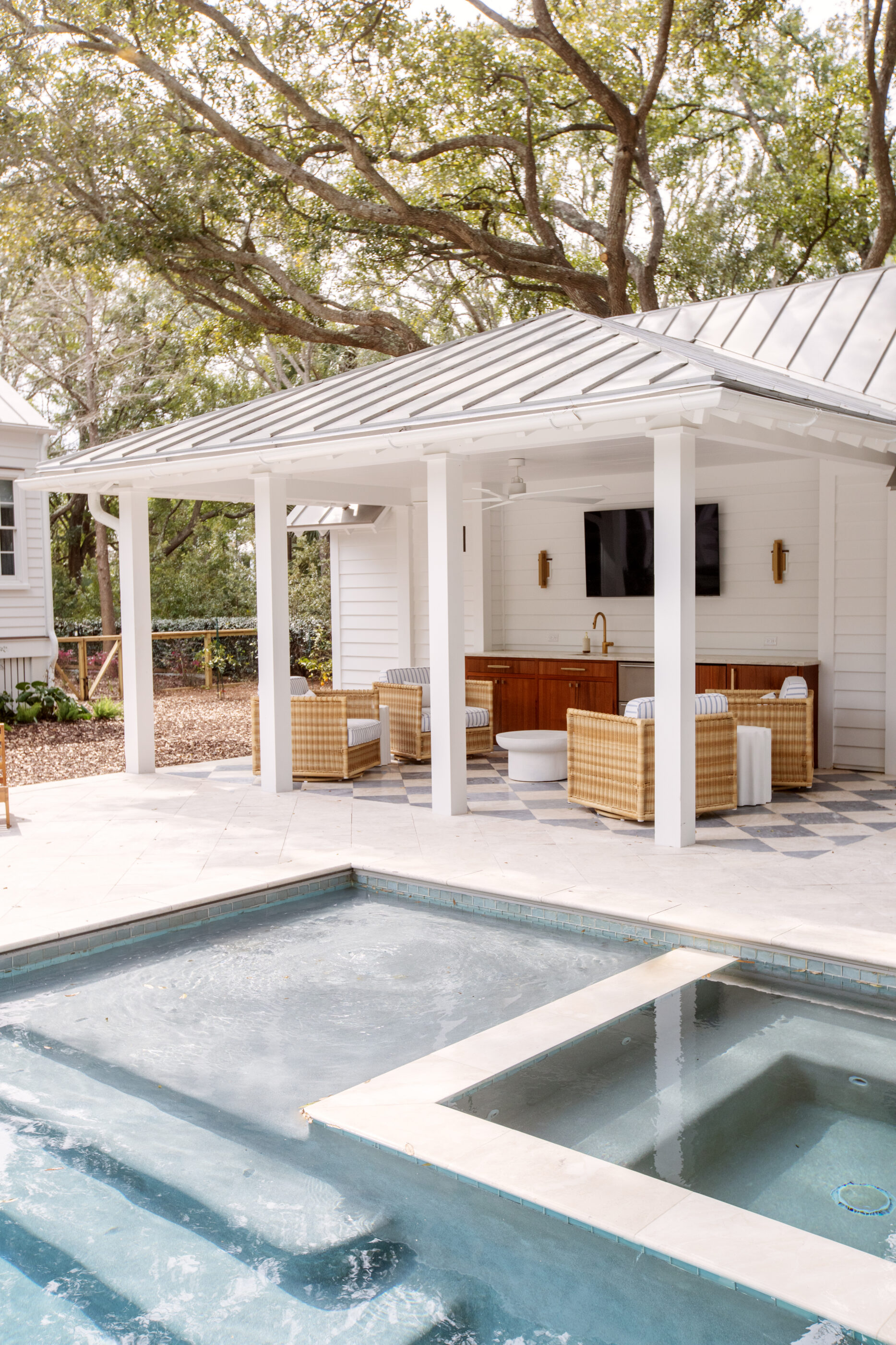 Elegant Charleston pool cabana with rattan outdoor furniture, metal roof, white columns, and luxury coastal outdoor living design.