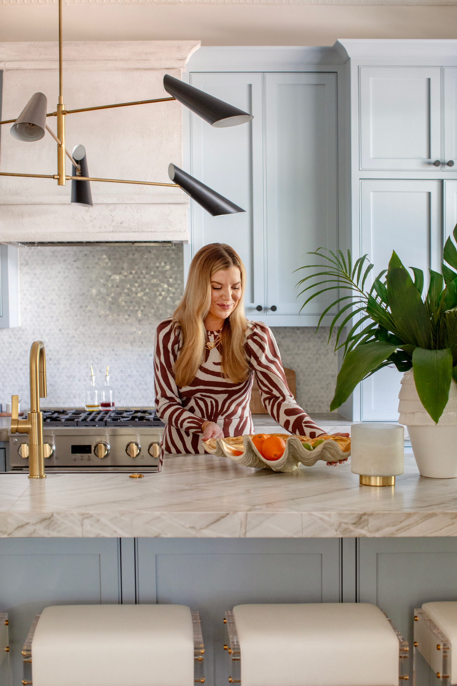 Luxury coastal kitchen with blue cabinetry, marble island, brass fixtures, designer lighting, and curated home decor accents.