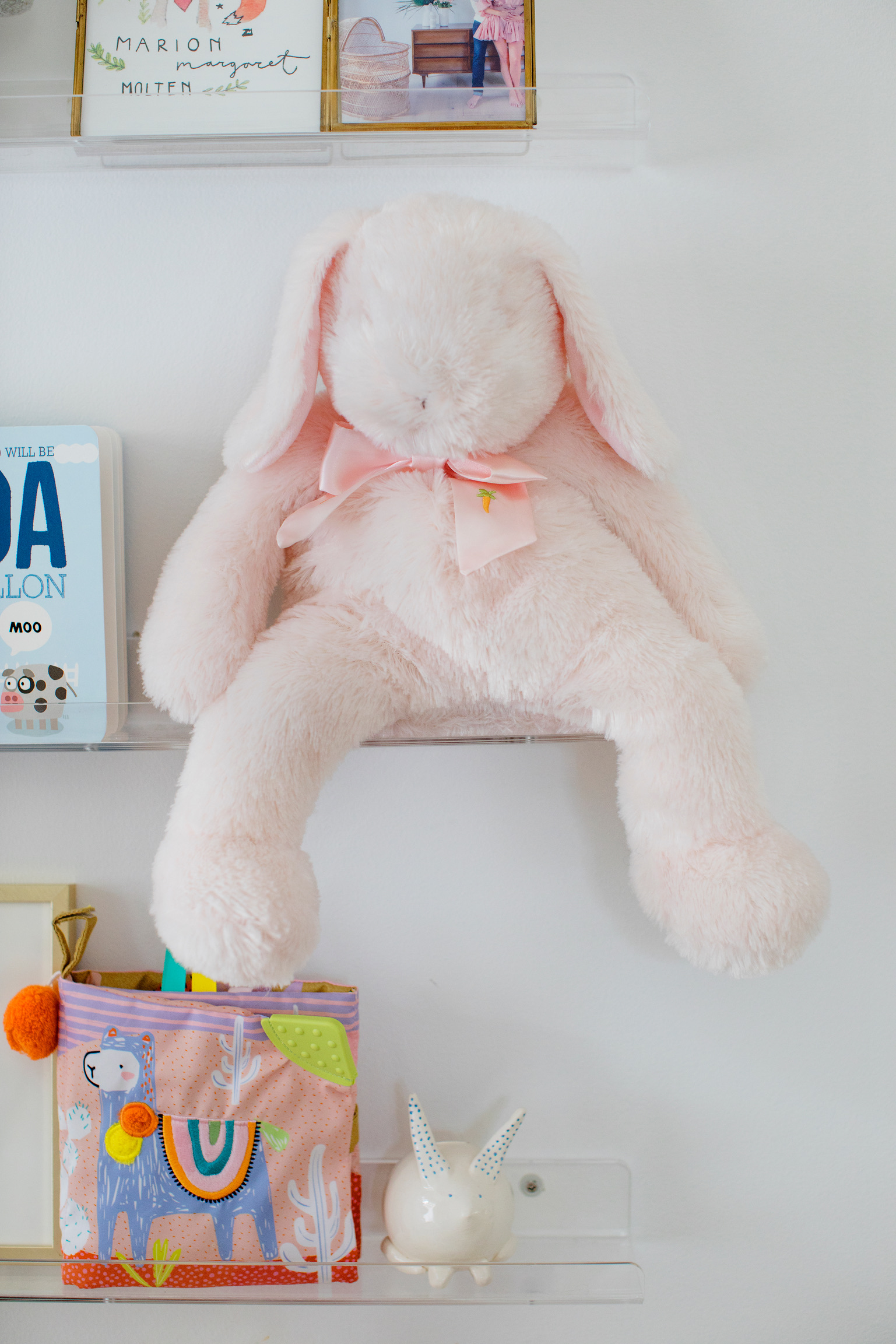 Kids room shelf styling with pink stuffed bunny, children’s books, framed art, and playful nursery decor.