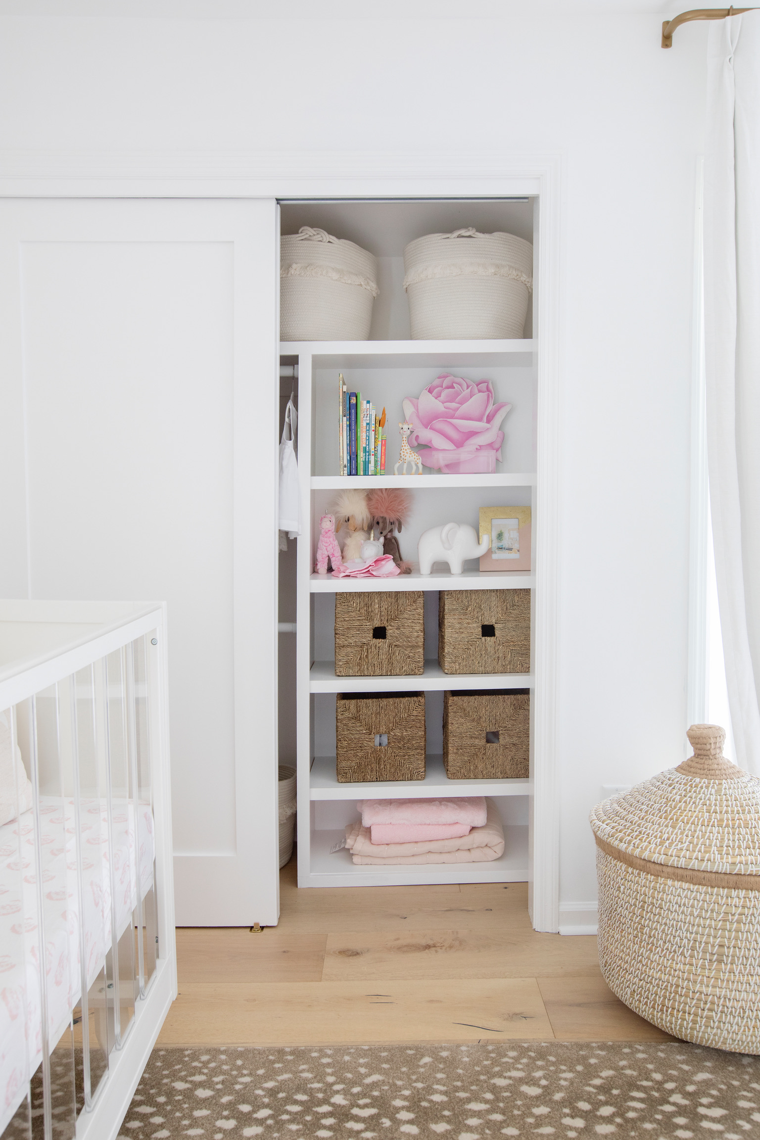Organized nursery closet with woven storage baskets, children’s books, folded blankets, toys, and neutral kids room decor.