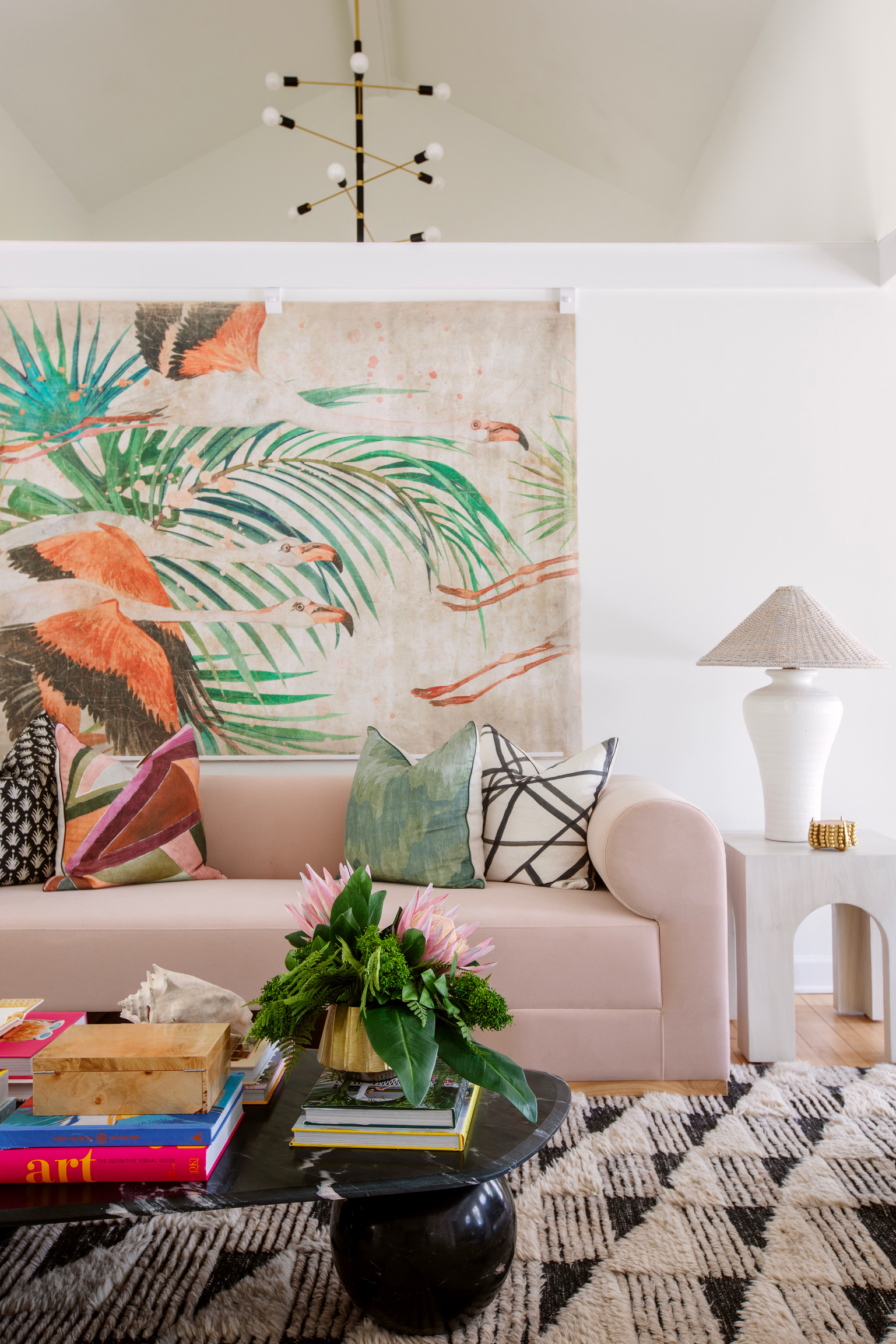 Colorful living room with pink sofa, tropical wall art, layered pillows, textured rug, and styled coffee table decor.