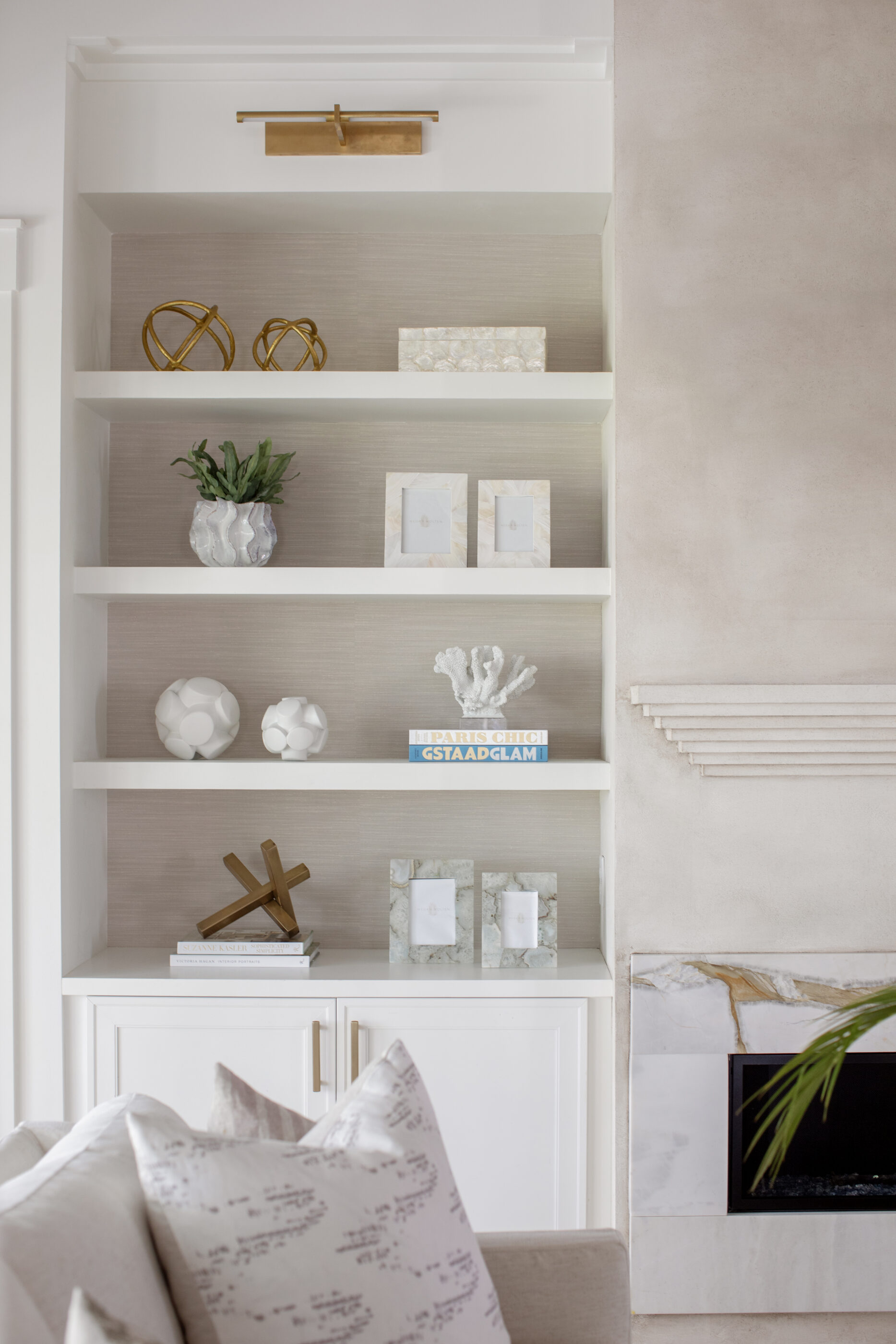 Built-in living room shelves styled with neutral decor, books, coral, gold accents, and a marble fireplace.