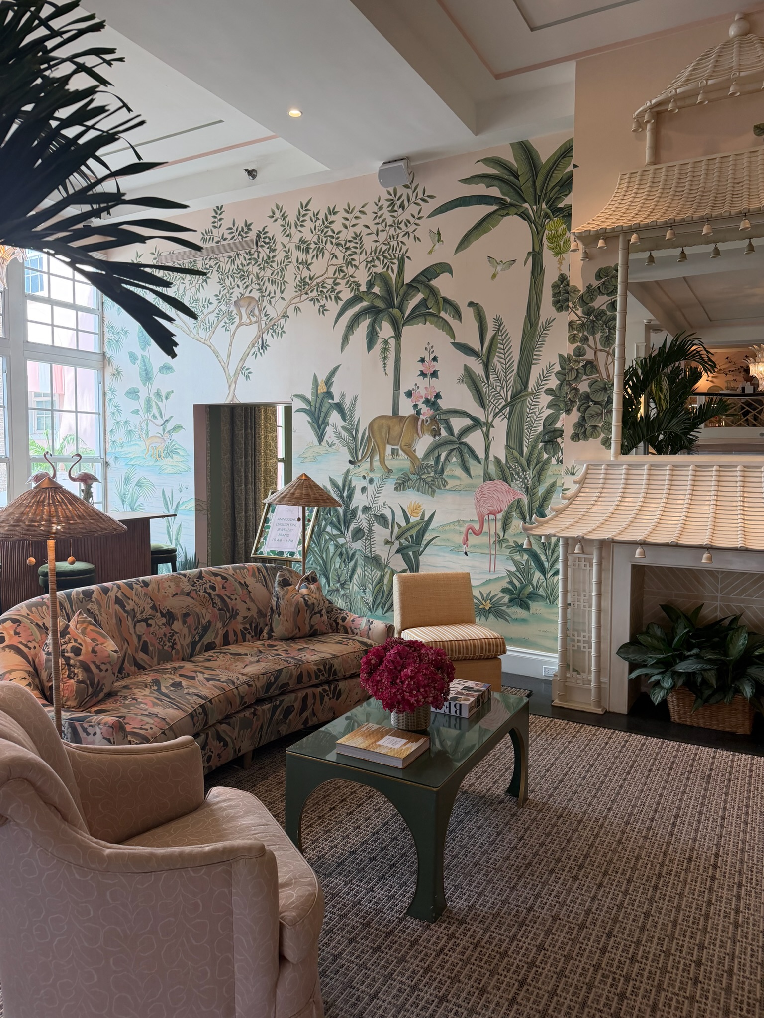 Tropical lounge with mural wallpaper, patterned sofa, rattan lighting, green coffee table, and layered botanical details.
