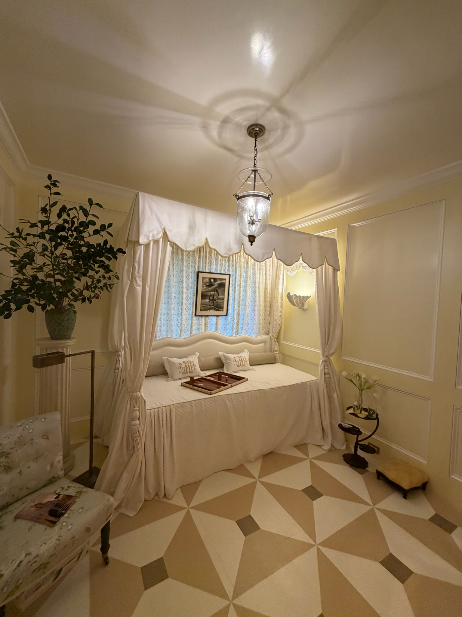 Soft yellow bedroom with a canopy daybed, scalloped fabric detail, painted geometric floor, and vintage-inspired lighting.