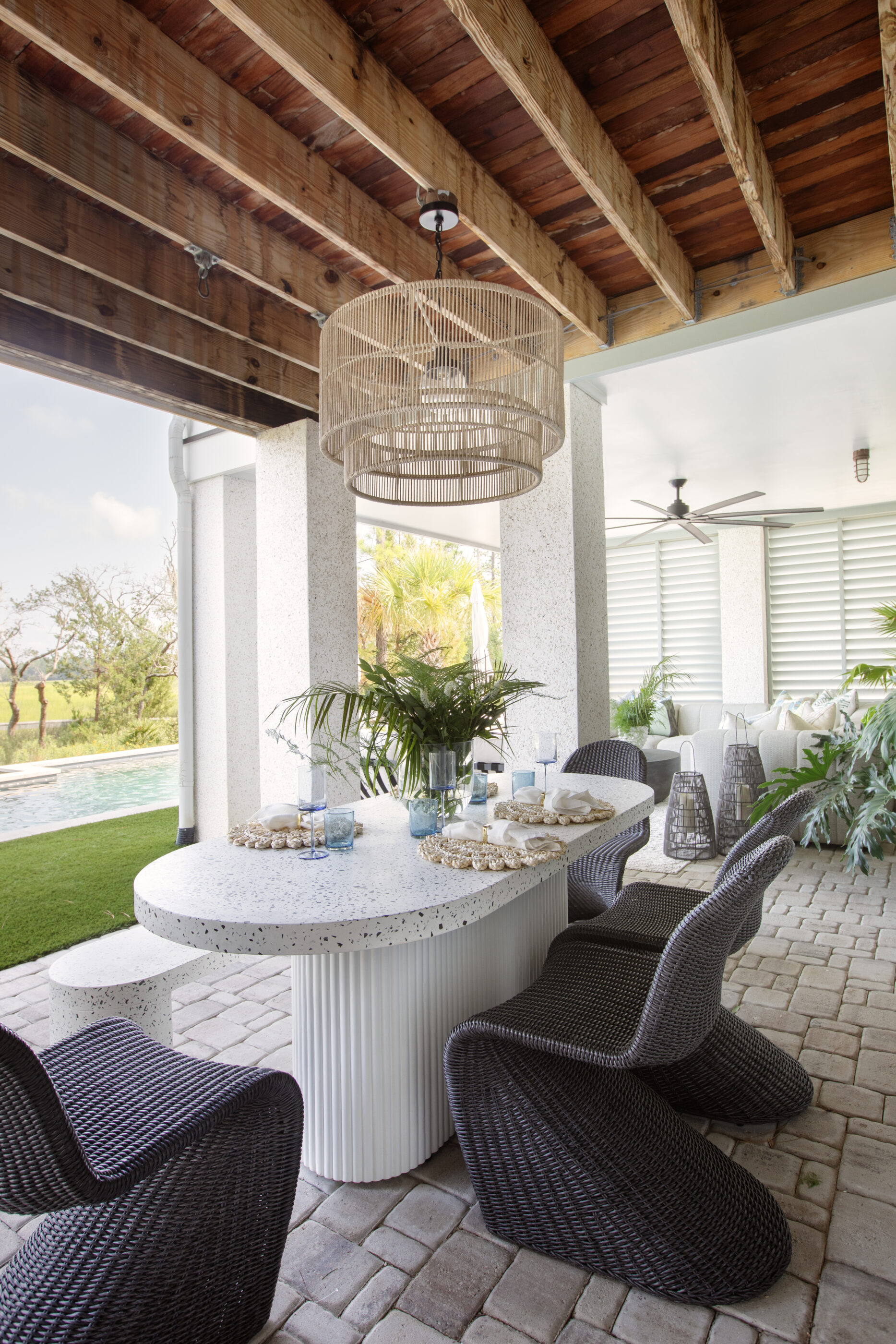 Covered outdoor dining space with woven chairs, a terrazzo-style table, tropical greenery, and breezy details suited to a Georgia coastal home.