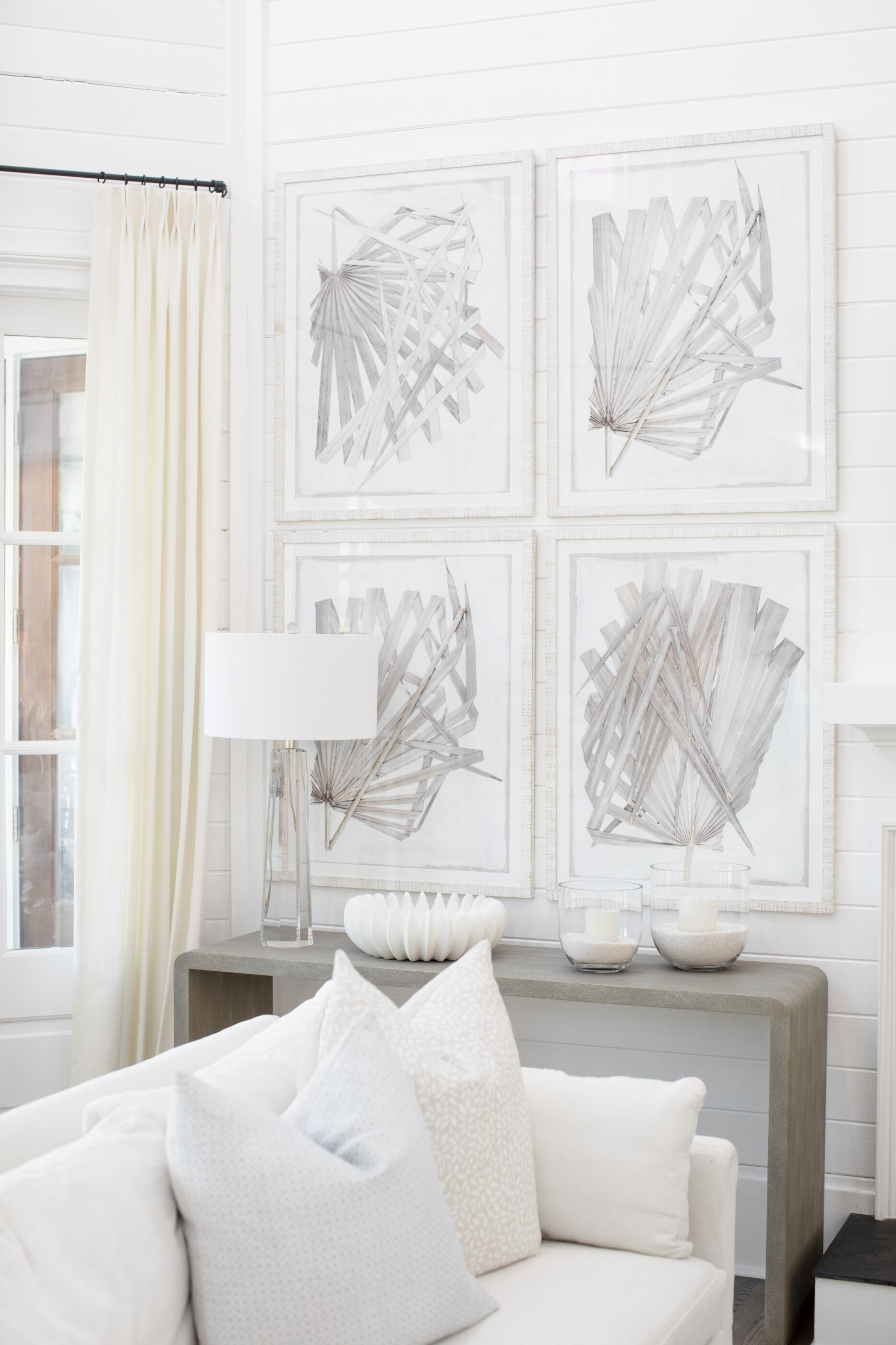Bright neutral living room with framed botanical artwork, soft curtains, decorative pillows, and a styled console table.