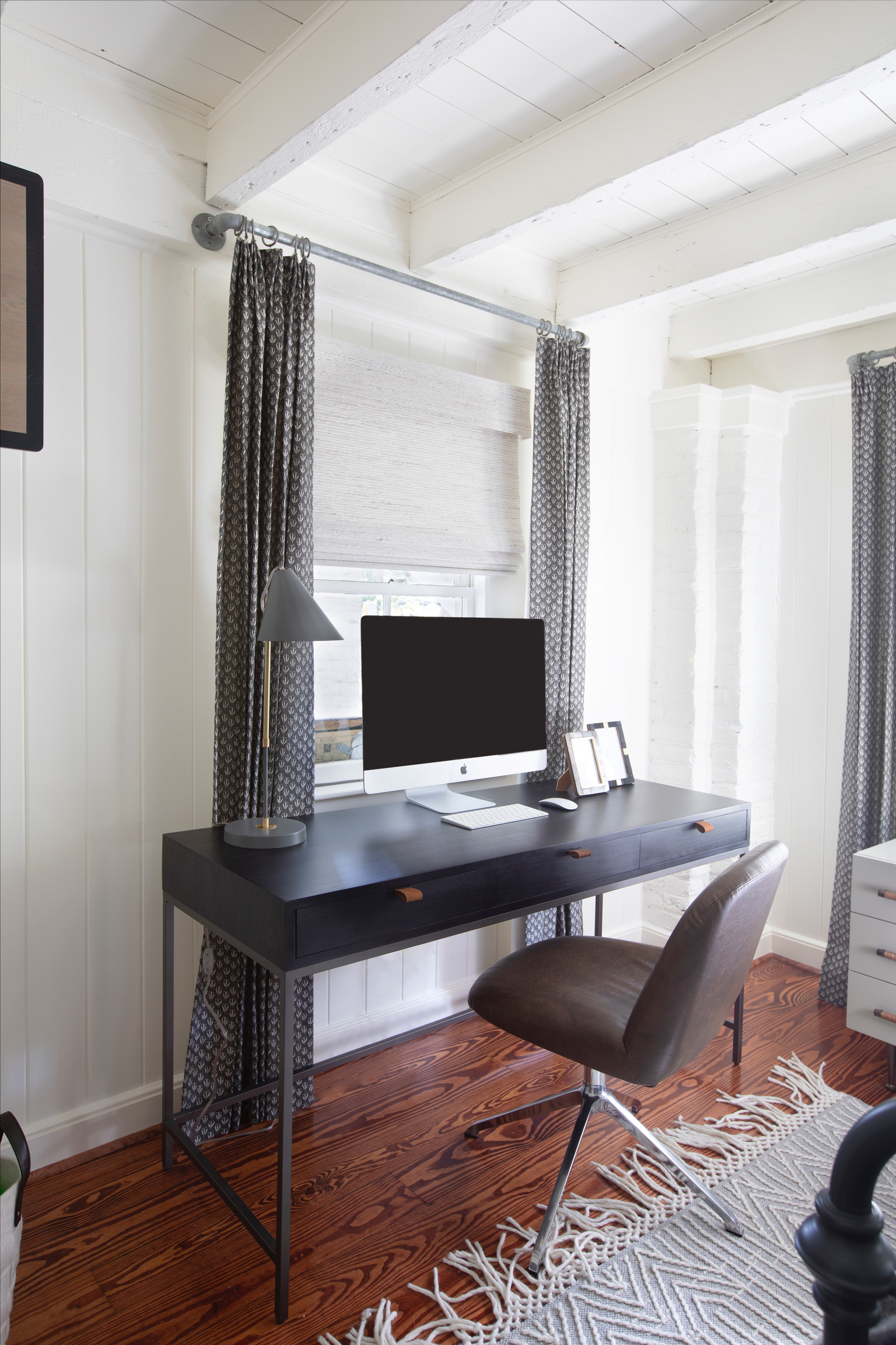 Small home office workspace with a black desk, computer, patterned curtains, and modern desk chair