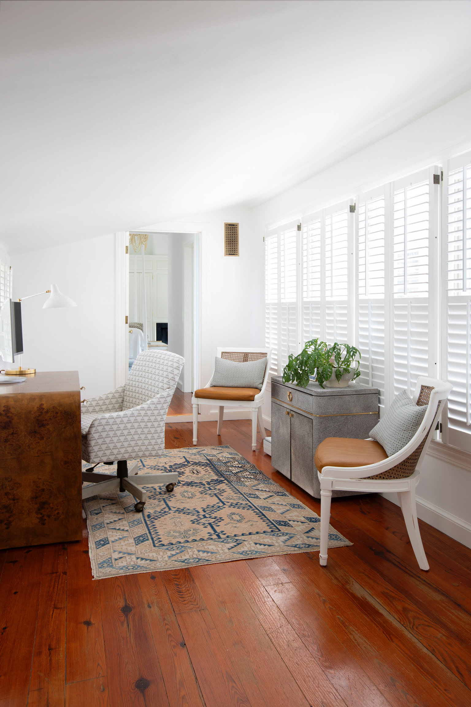 Bright home office with a wood desk, patterned rug, seating area, and natural light