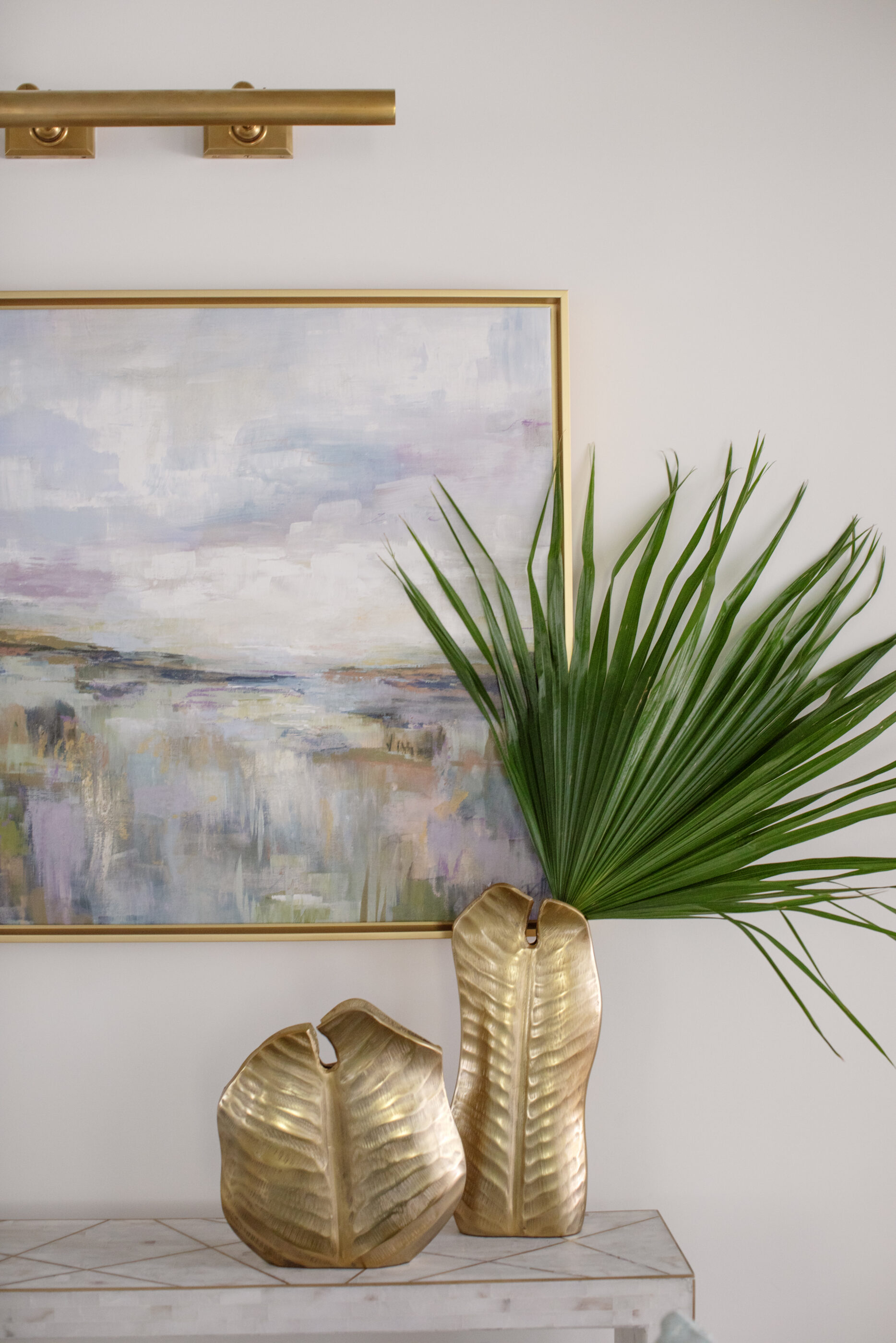 Wall decor ideas with framed abstract art, sculptural gold vases, greenery, and brass picture light