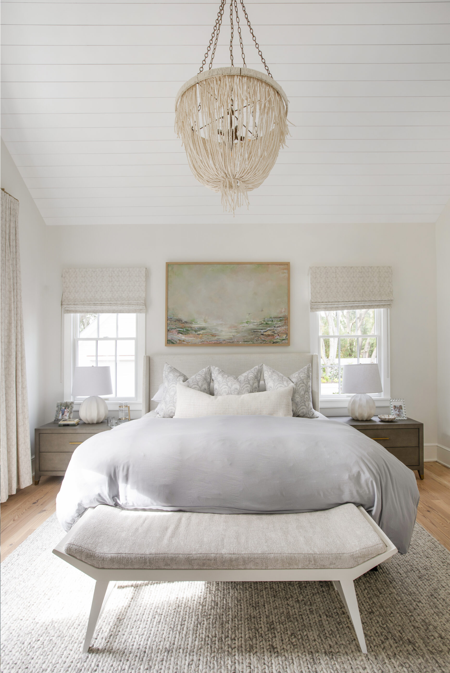 Bedroom wall decor with large framed artwork above a neutral upholstered bed in a bright coastal bedroom
