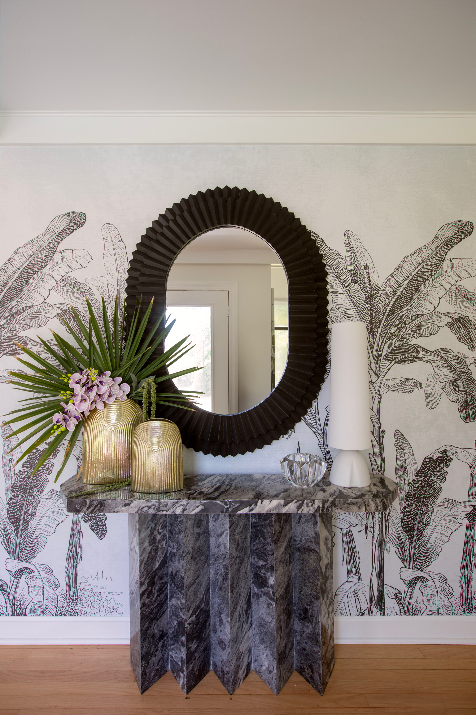 Sculptural stone console and black statement mirror styled against black-and-white botanical wallpaper.