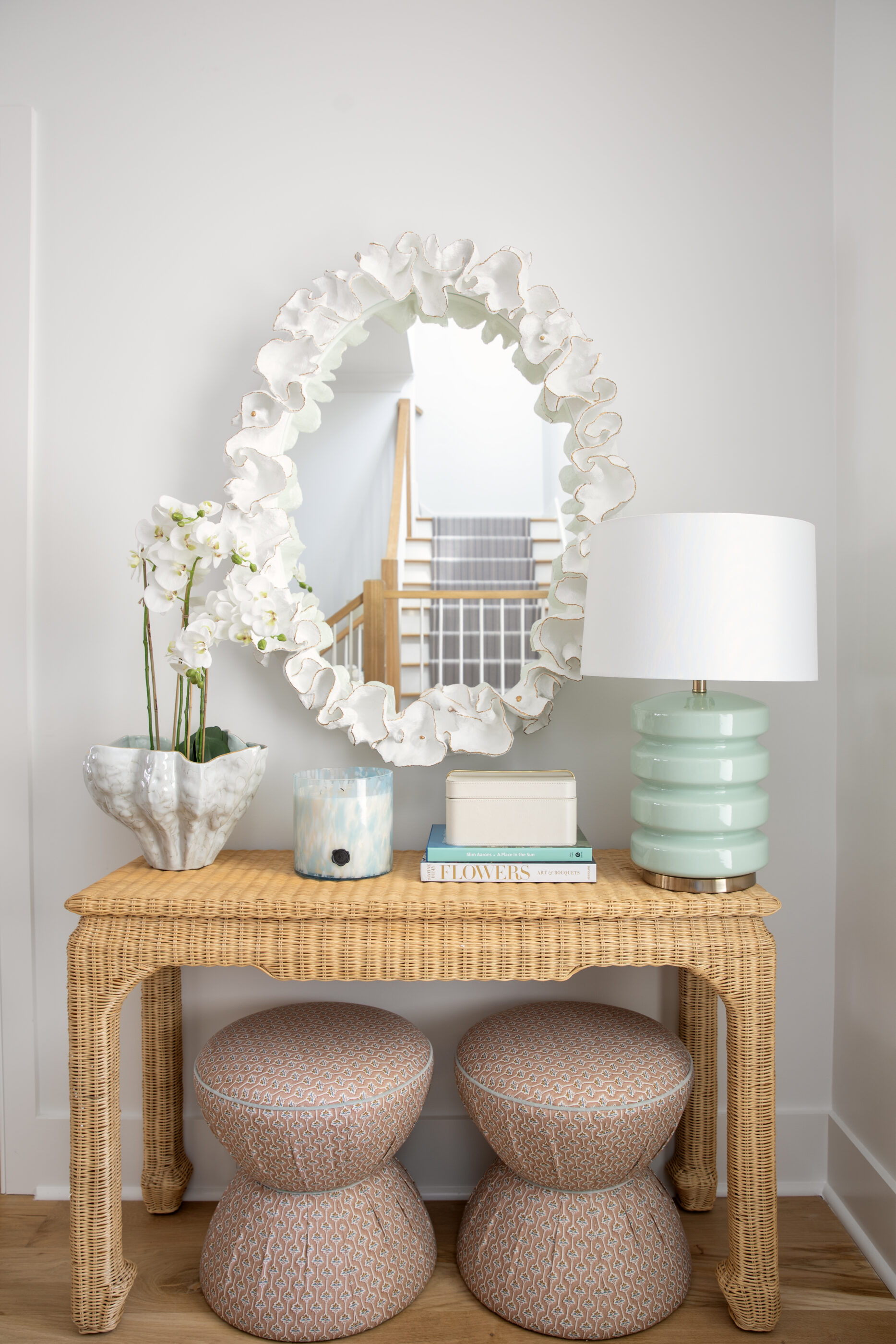 Wall decor ideas with a statement mirror above a woven console table styled with a lamp, flowers, and decorative accents