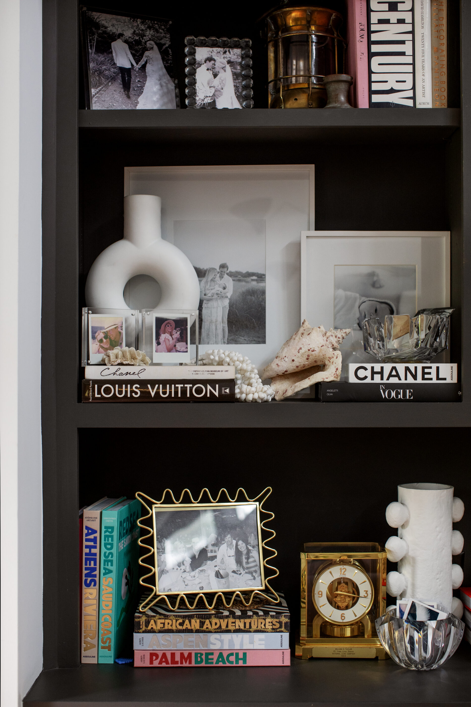 Dark built-in bookshelves styled with family photos, fashion books, sculptural decor, keepsakes, and collected objects.