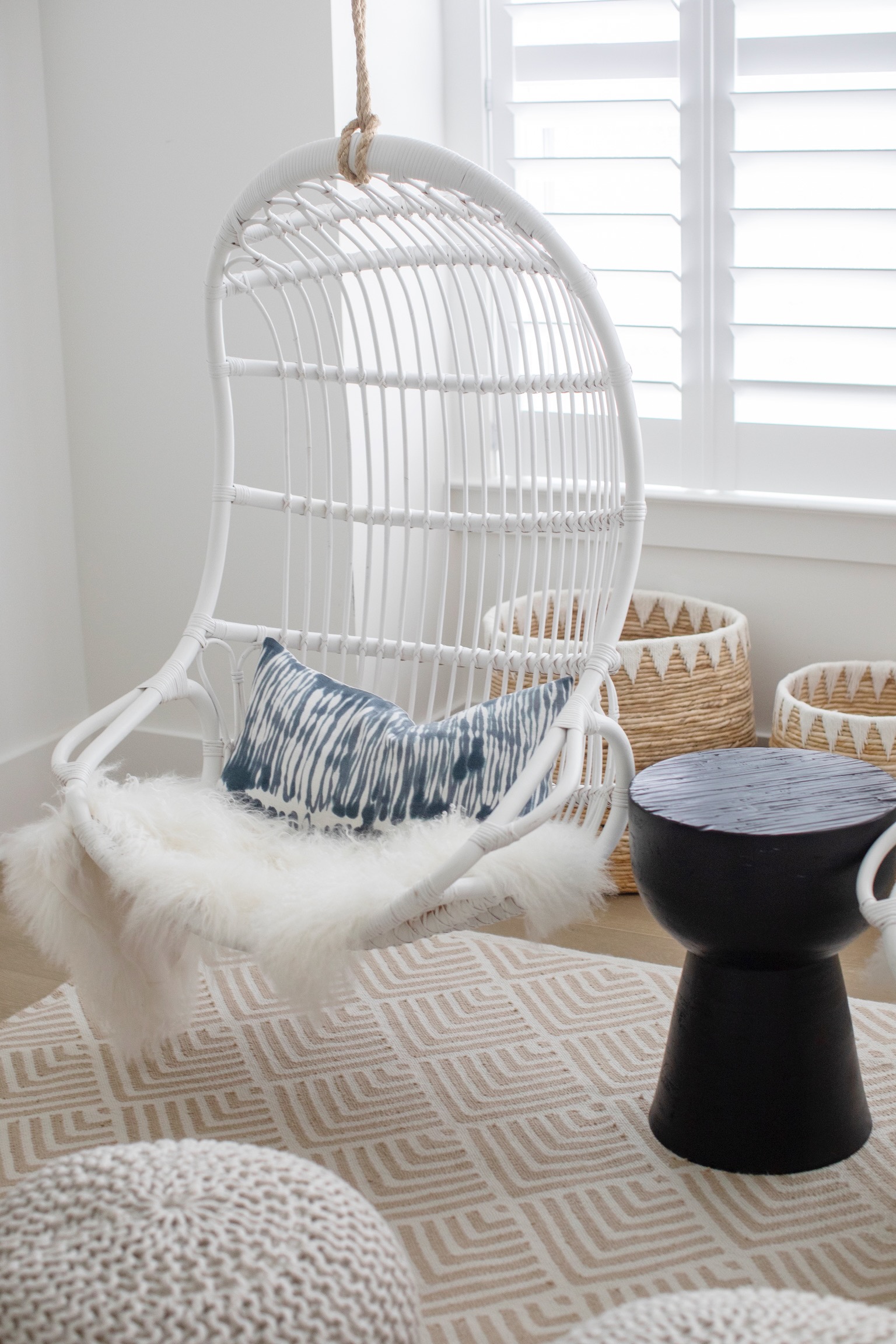 Cozy dorm room decor with white hanging chair, blue accent pillow, woven baskets, and small side table