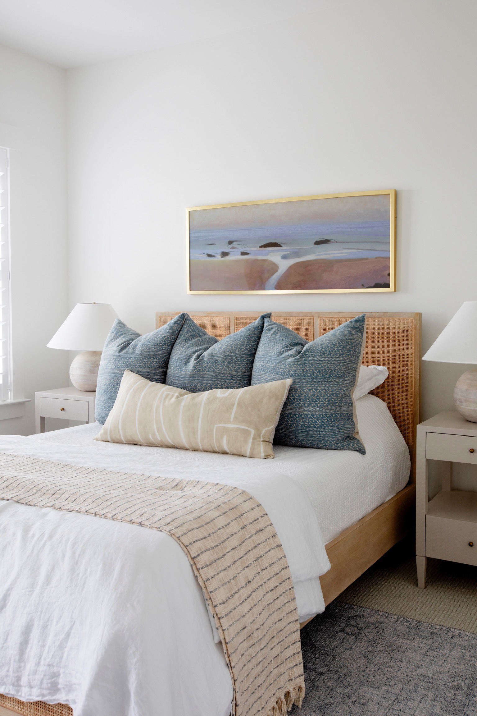 Coastal dorm room decor ideas with blue pillows, neutral bedding, woven headboard, and framed wall art