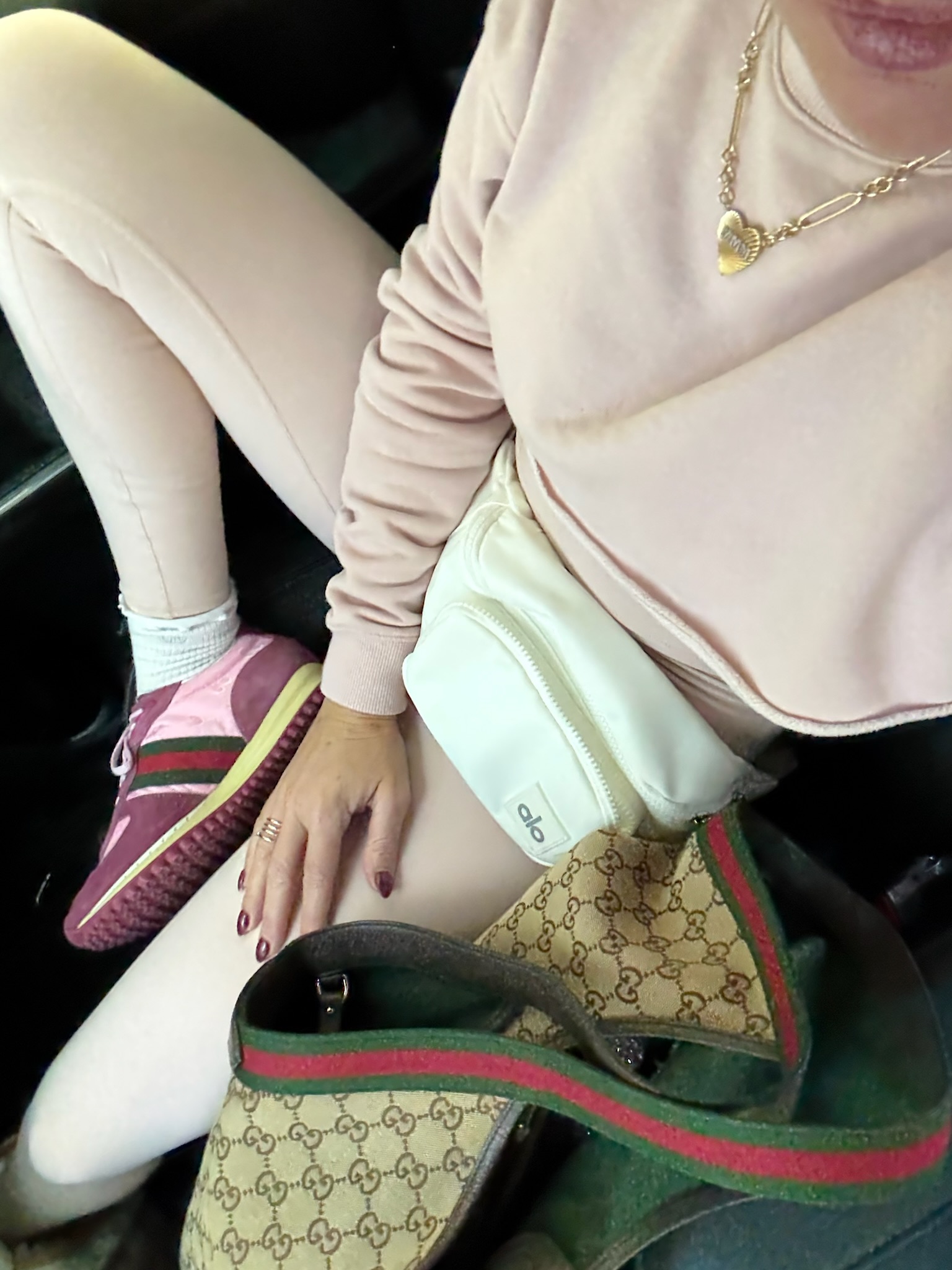Close-up of a comfortable travel outfit with blush athleisure, pink Gucci sneakers, an Alo belt bag, and a Gucci tote.