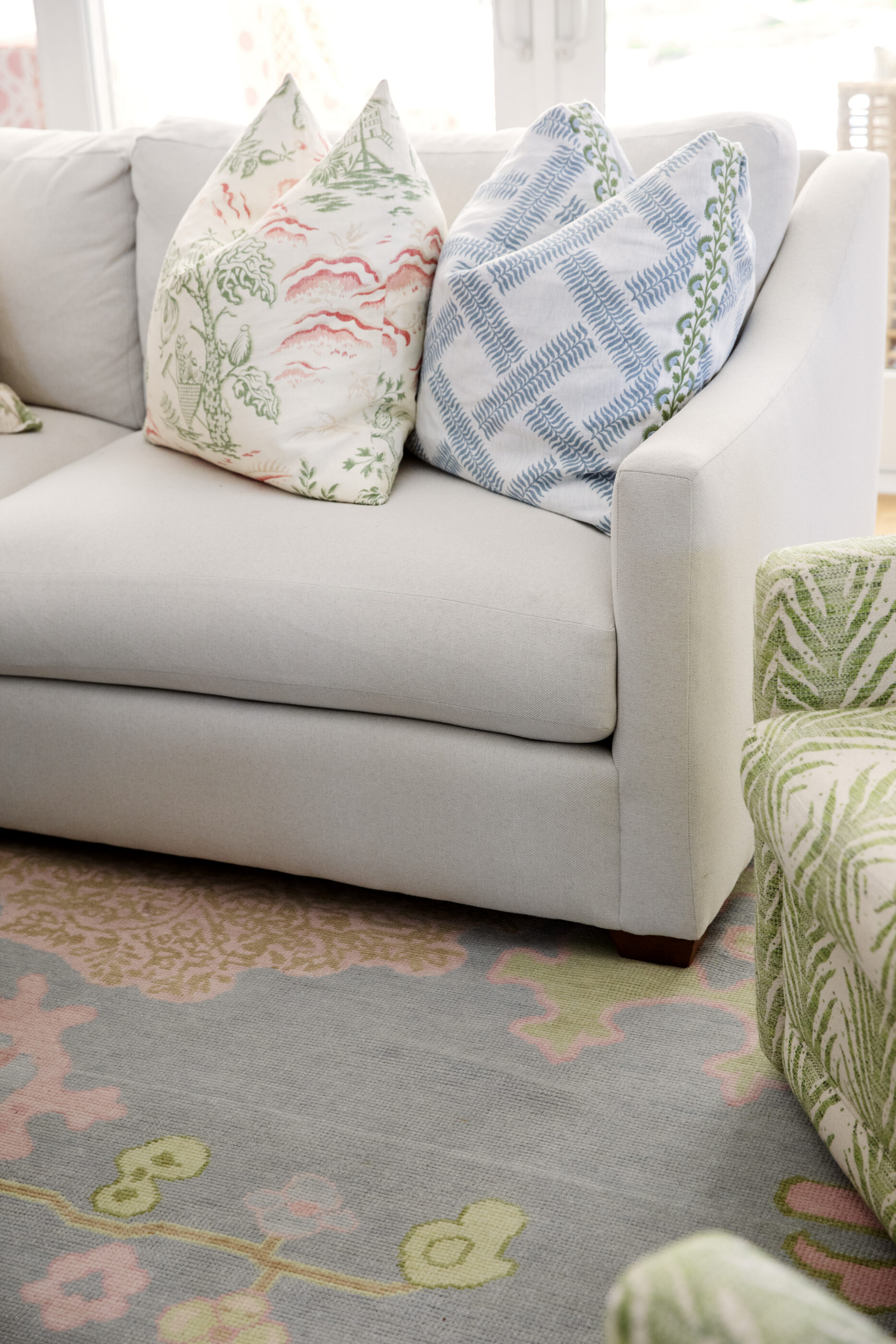 Coastal living room design featuring a neutral sofa, colorful botanical throw pillows, a pastel patterned area rug, and a green upholstered accent chair.